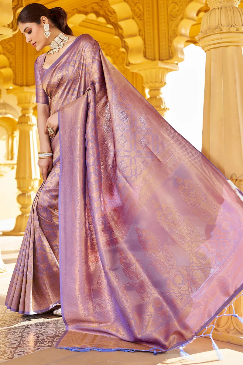 Woman in a purple saree standing in front of an ornate architectural background