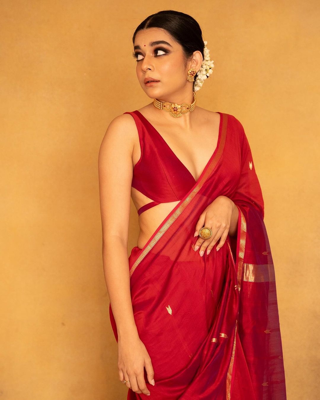 Woman in a red saree with gold accents holding a gold bag against