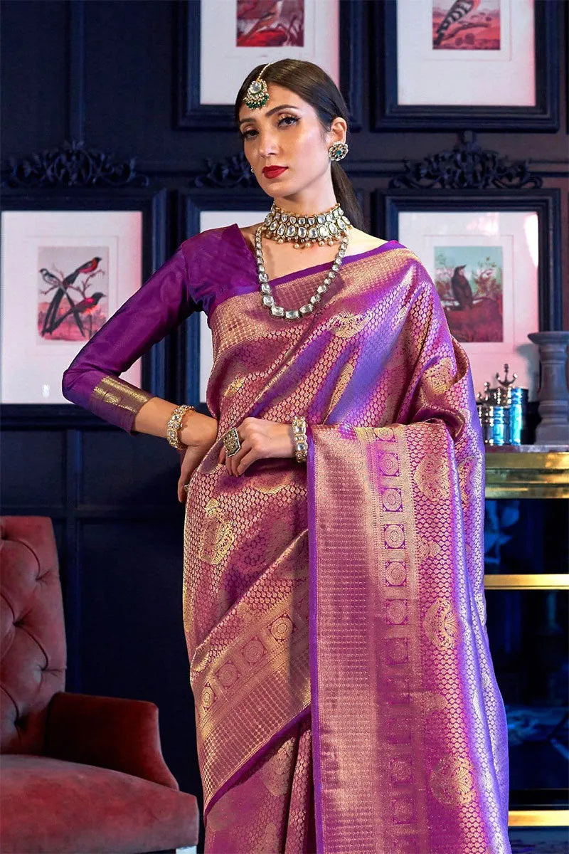 Woman in a purple saree with gold patterns in an elegant room.