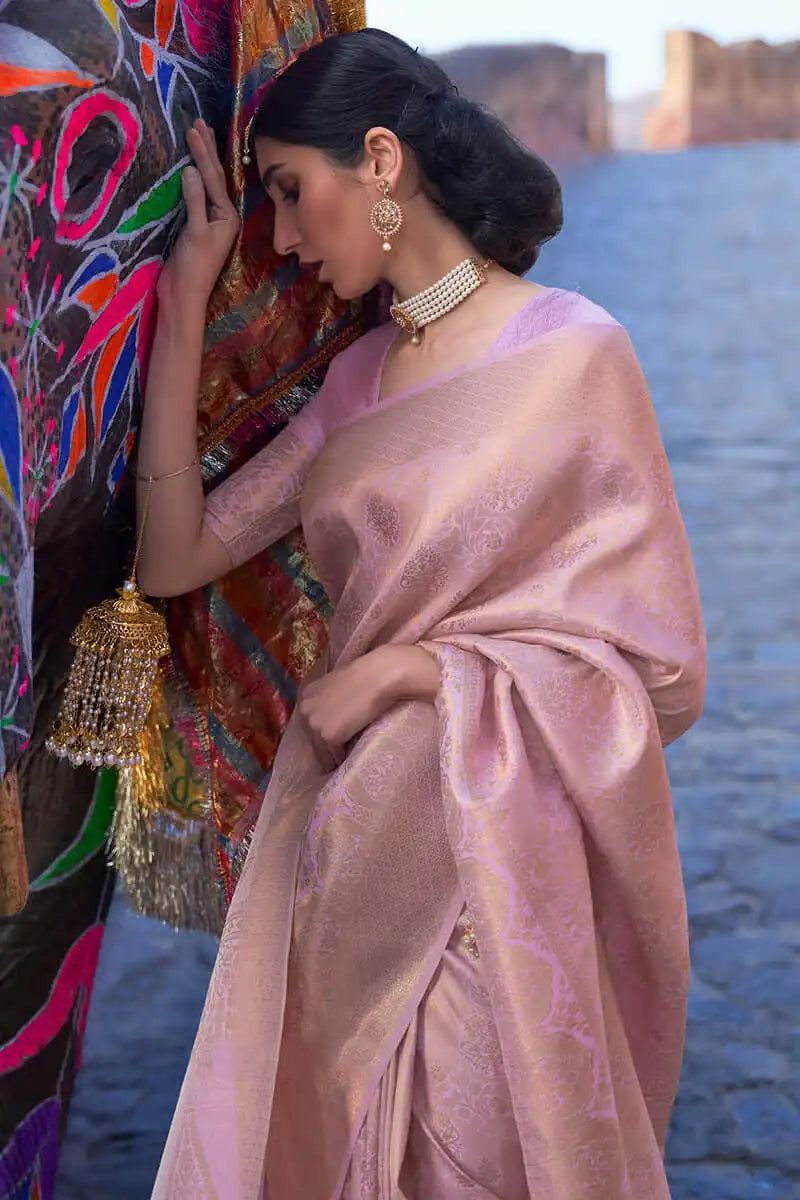 Woman in a pink saree with jewelry standing near a colorful wall.