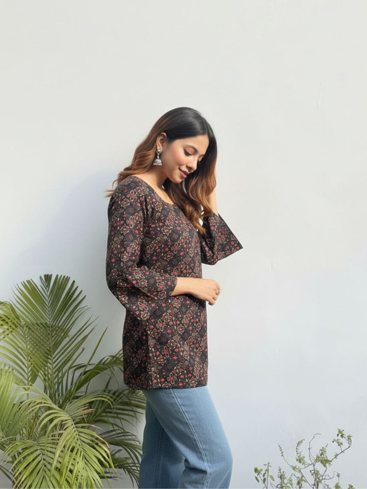 Woman wearing a floral blouse and jeans standing against a light background with plants.