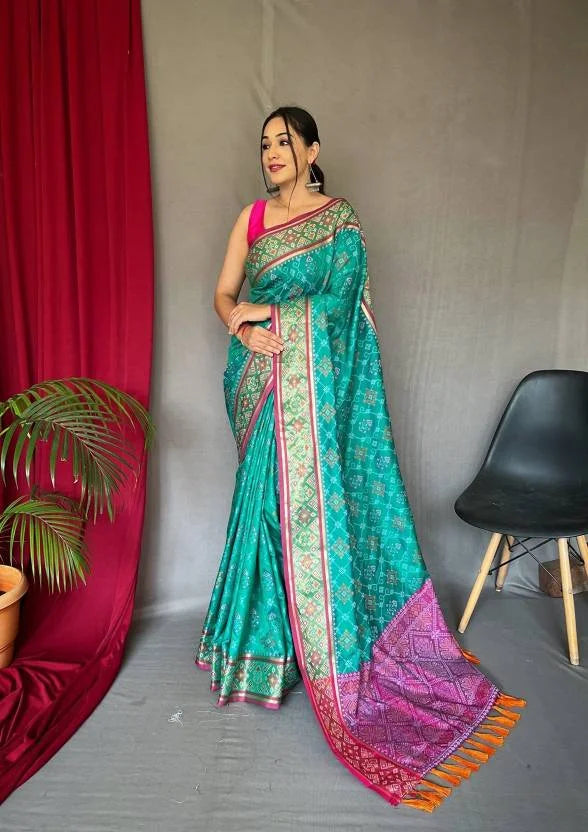 Woman wearing a green and pink saree with a red curtain and chair in the background