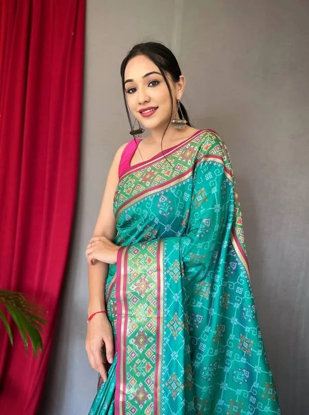 Woman wearing a green saree with a pink blouse against a gray wall.