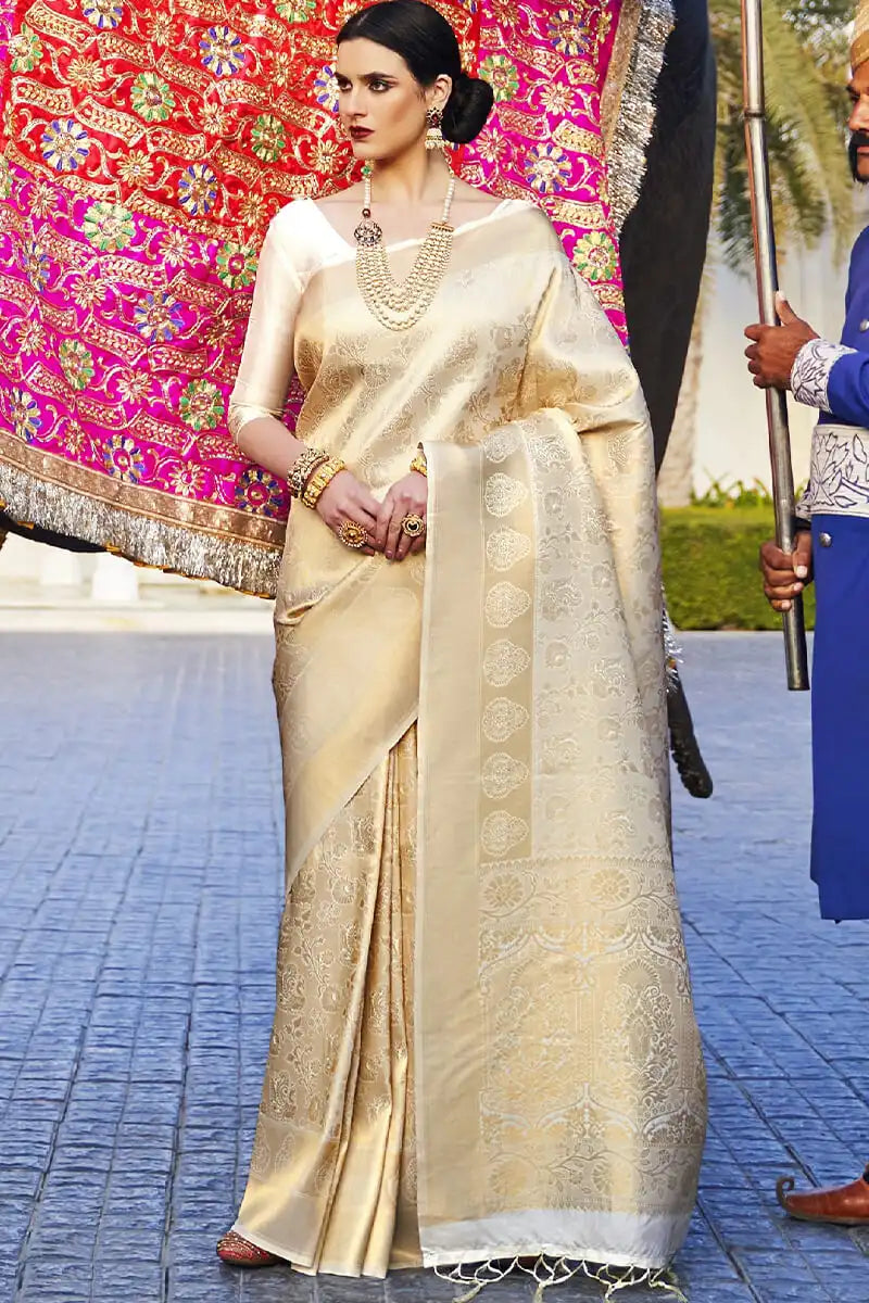 Woman in a traditional beige saree with gold details on a blue pavement.