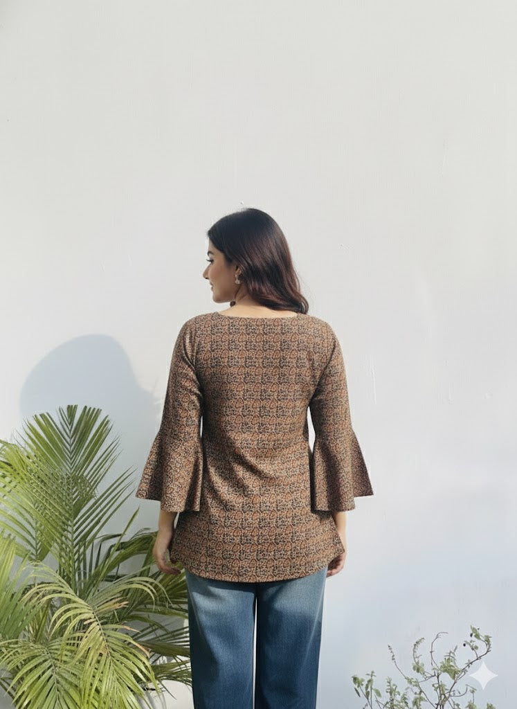 Person wearing a brown patterned jacket with a white background and green plants.