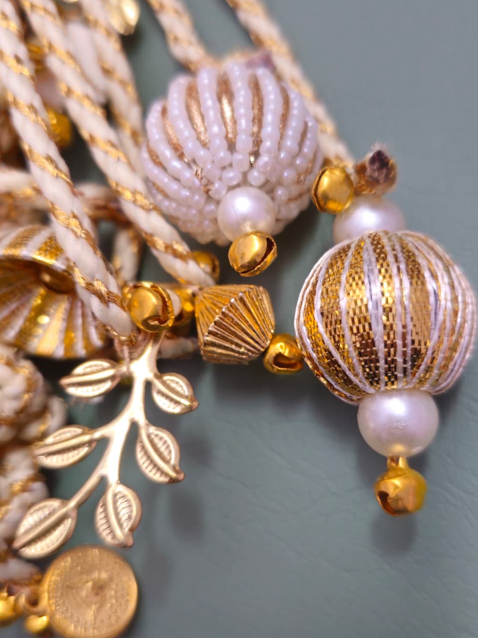 Close-up of a decorative necklace with gold and pearl beads on a light blue background