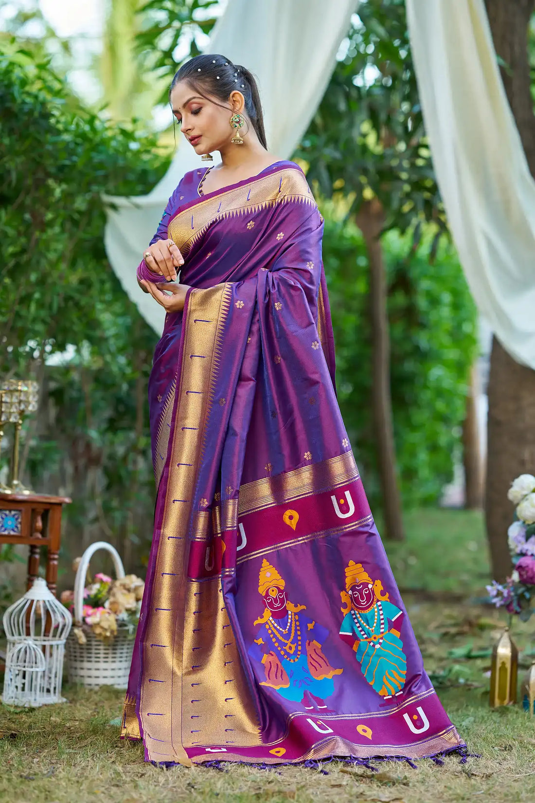 Woman wearing a traditional purple saree with gold border and temple design, standing outdoors.