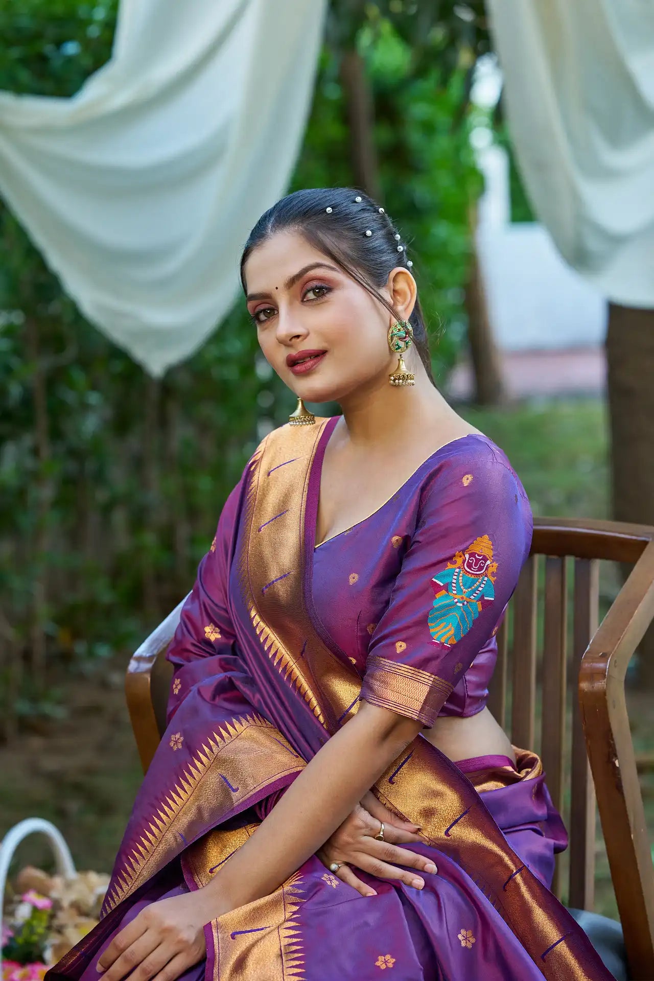 Woman in a purple saree with gold patterns sitting outdoors.