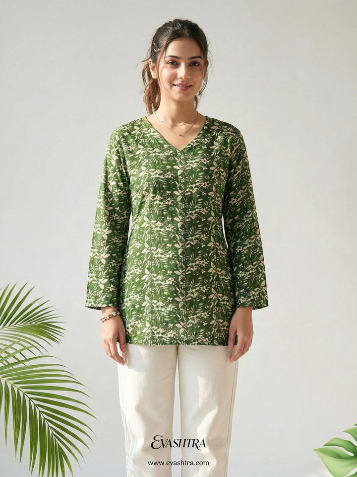 Woman wearing a green patterned top with white pants on a light gray background, featuring the brand 'Evashtra'.