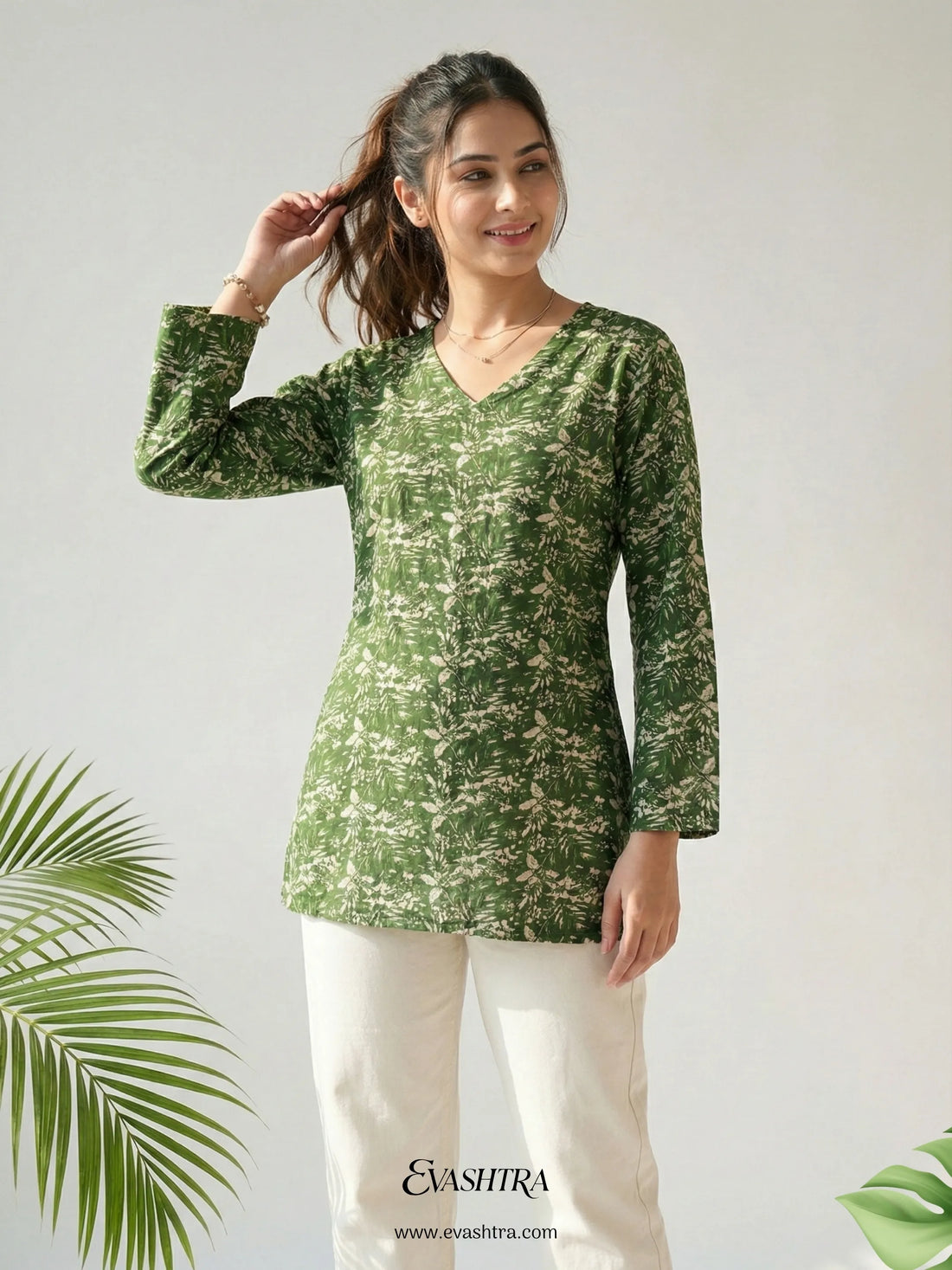 Woman wearing a green patterned top with white pants against a light background