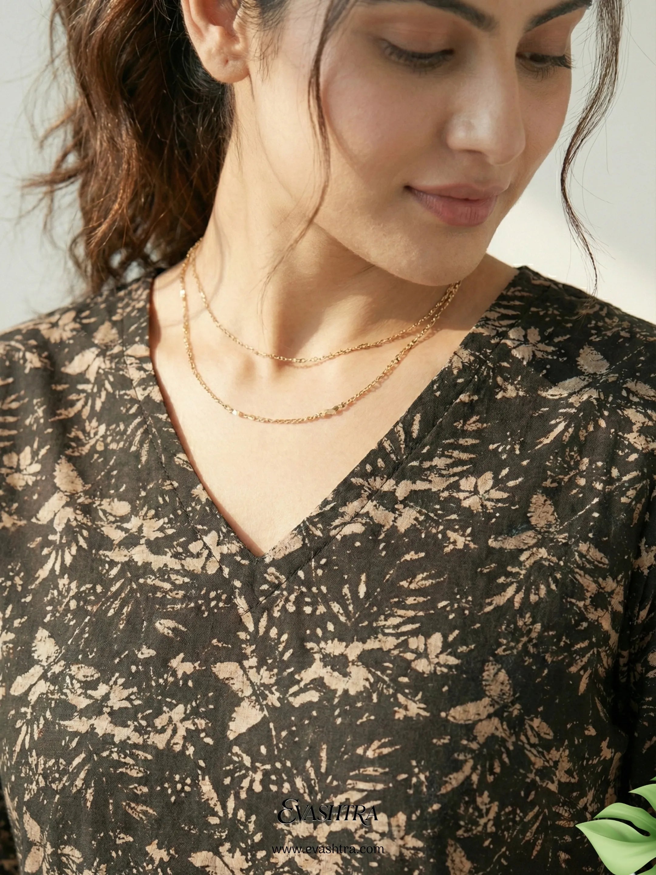 Woman wearing a black floral patterned top with layered gold necklaces.