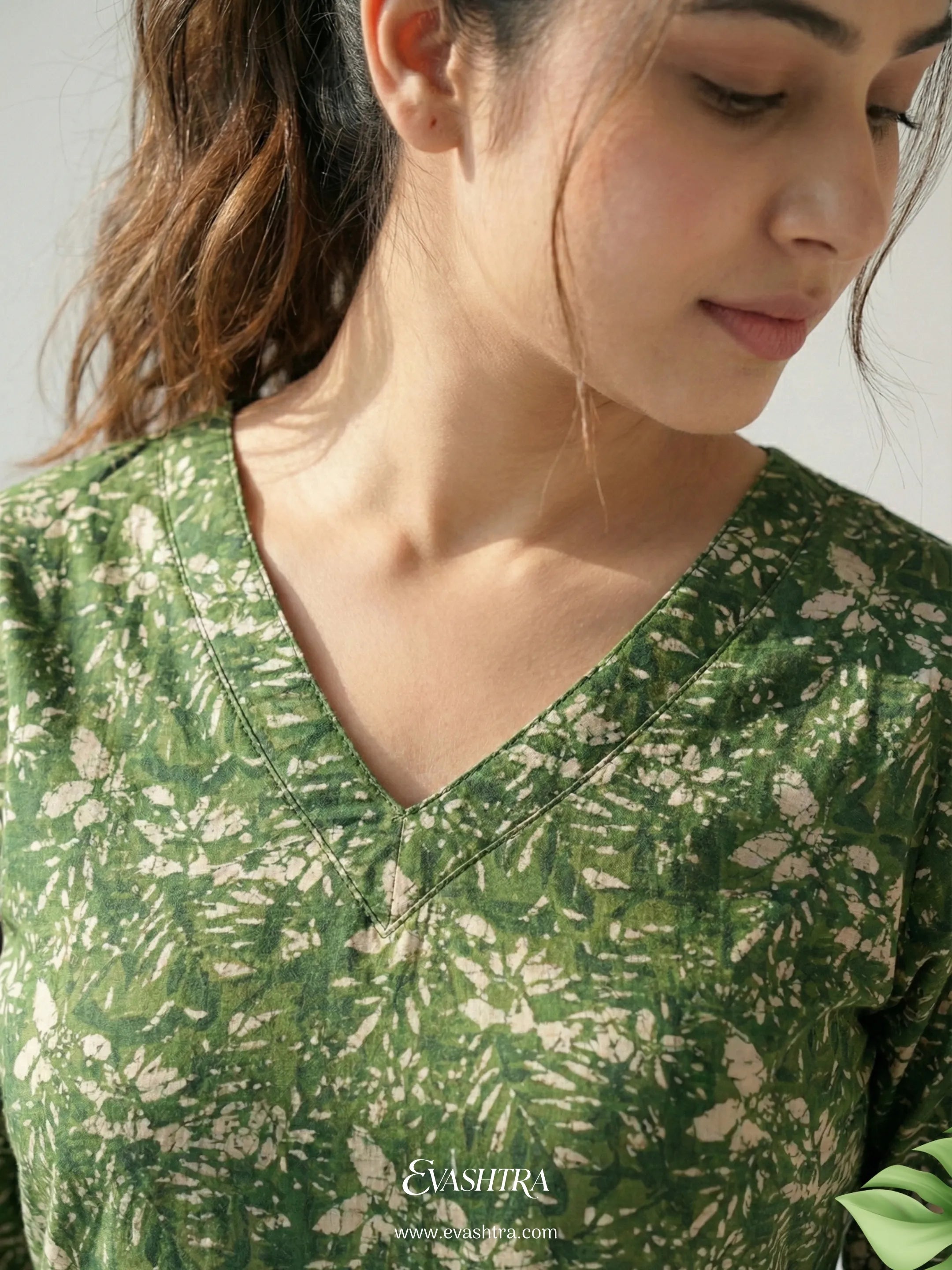 Woman wearing a green floral blouse with 'EvaShri' branding.