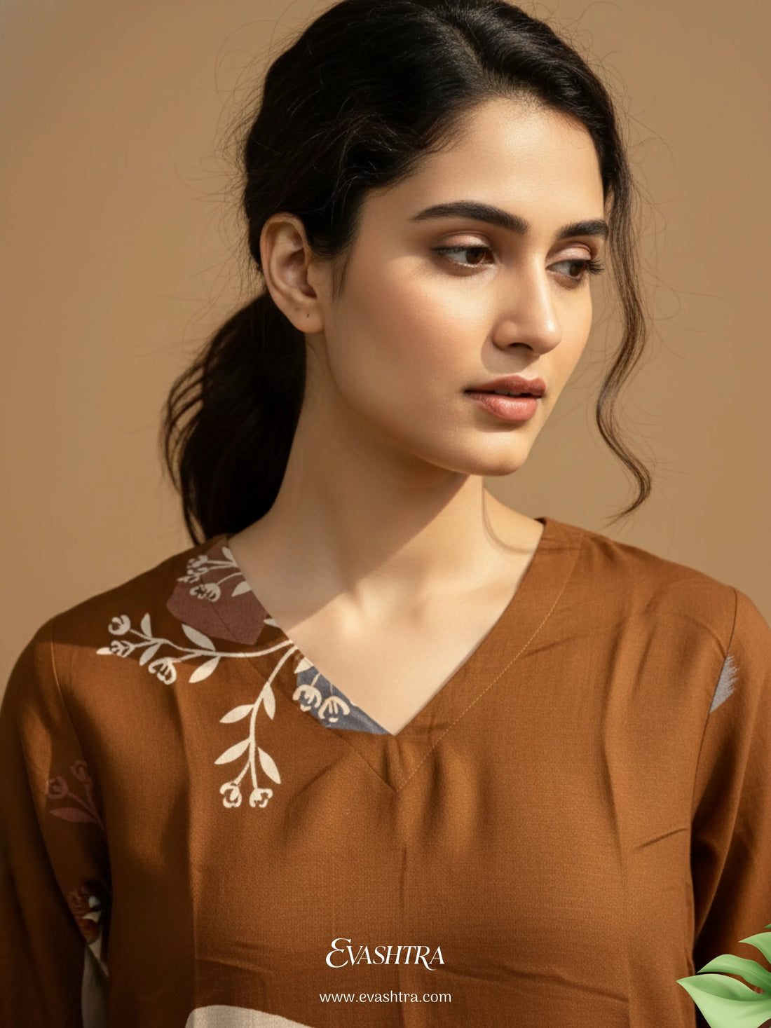 Woman wearing a brown embroidered top with a plain background
