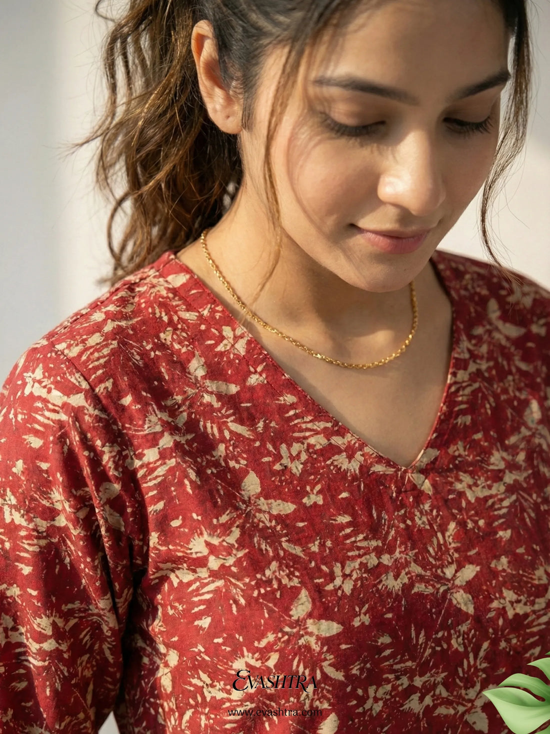 Woman wearing a red floral blouse with a gold necklace, looking down.