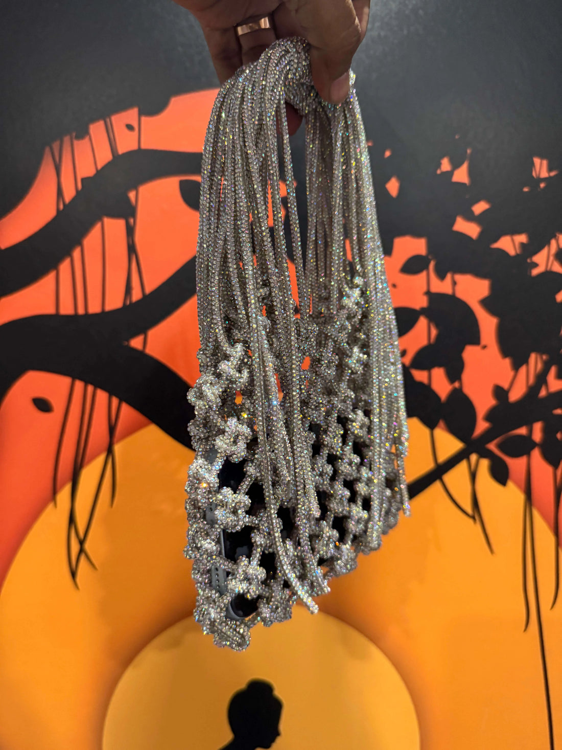 Silver beaded necklace held by a hand against a colorful abstract background