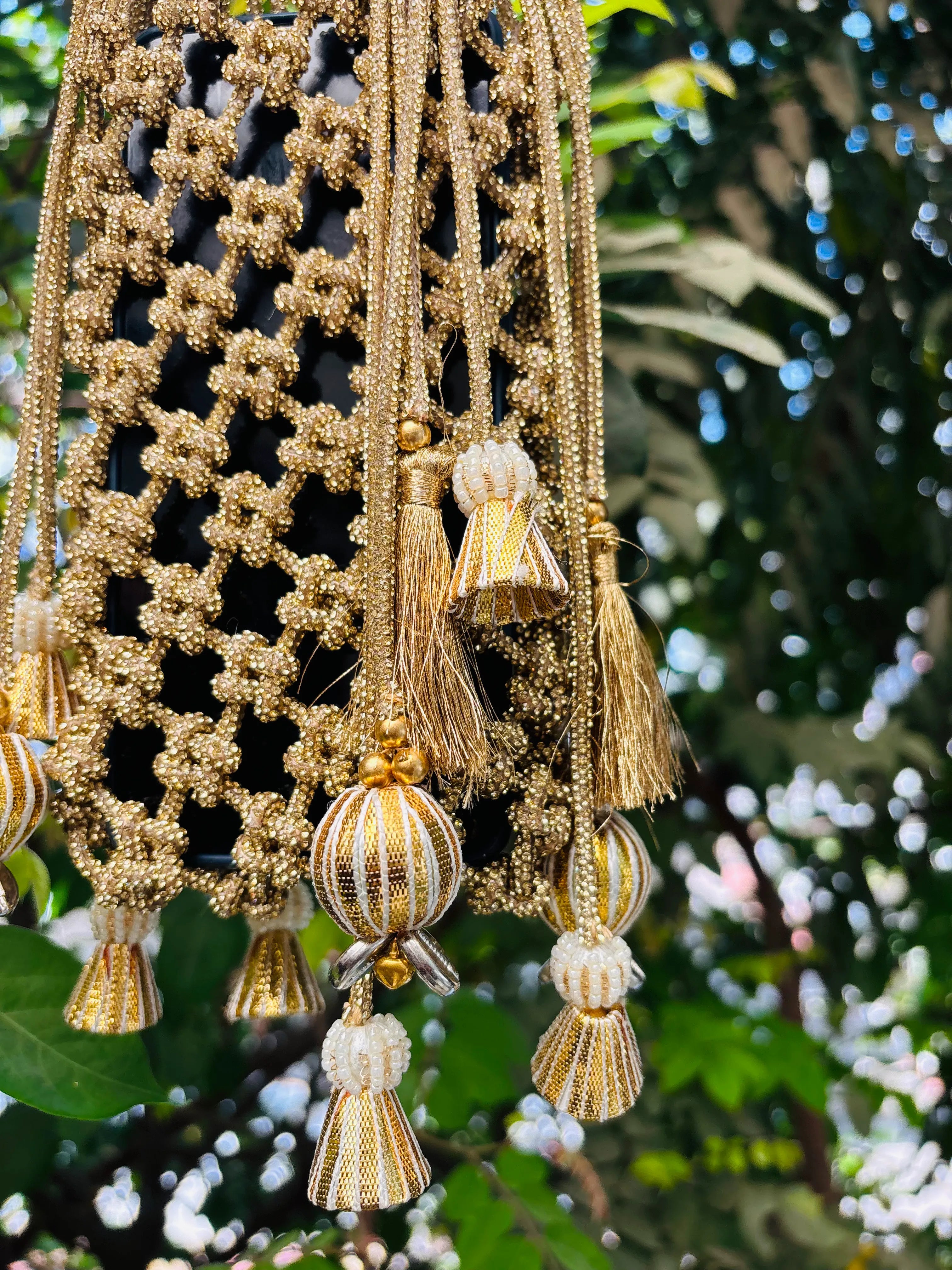 Decorative hanging with gold tassels and beads against a blurred natural background