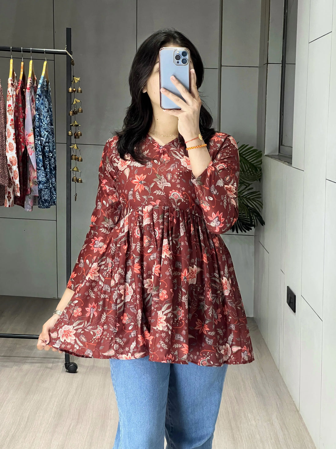 Person wearing a red floral dress and blue jeans taking a mirror selfie.