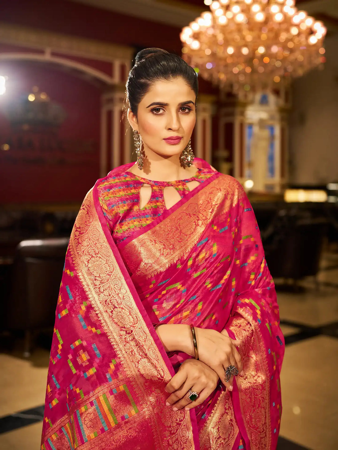 Woman in a pink saree with intricate patterns in a decorated indoor setting