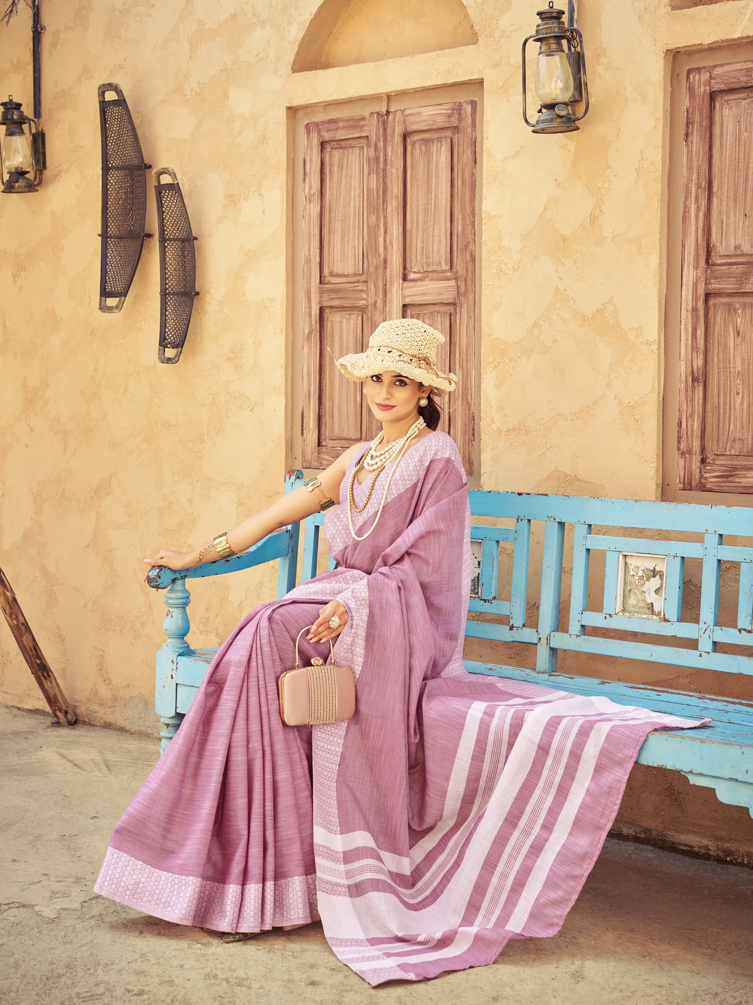 Woman in a pink saree sitting on a blue bench in a rustic setting.