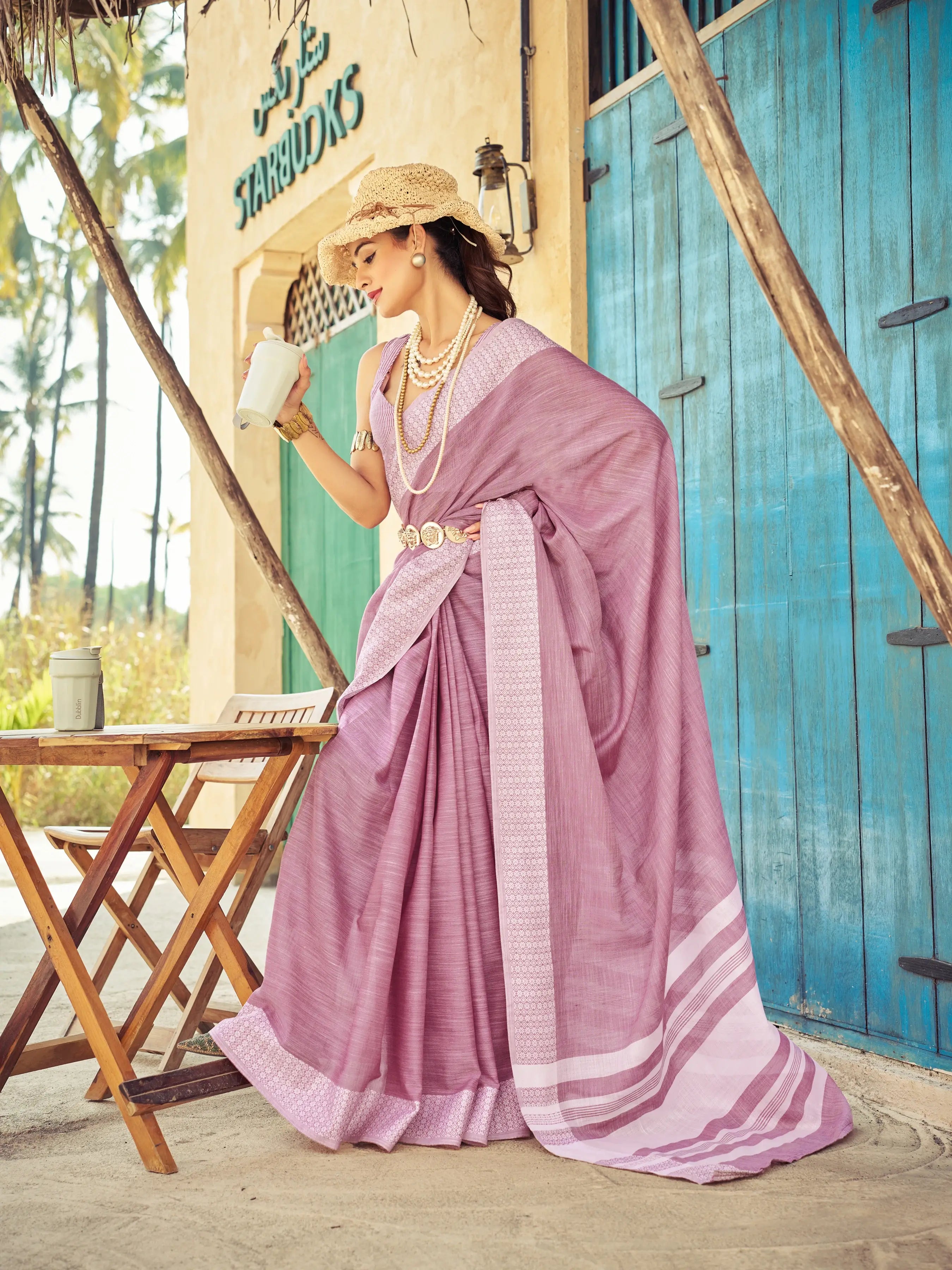 Woman in a pink saree standing in front of a blue door with 'Harbours' sign.