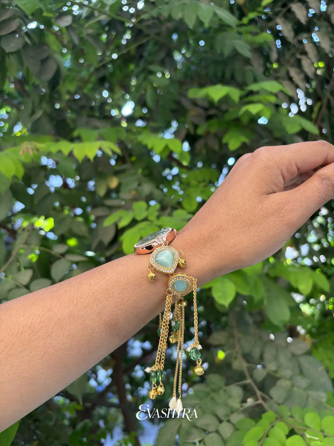 Gold bracelet with green stones on a wrist against a green leafy background