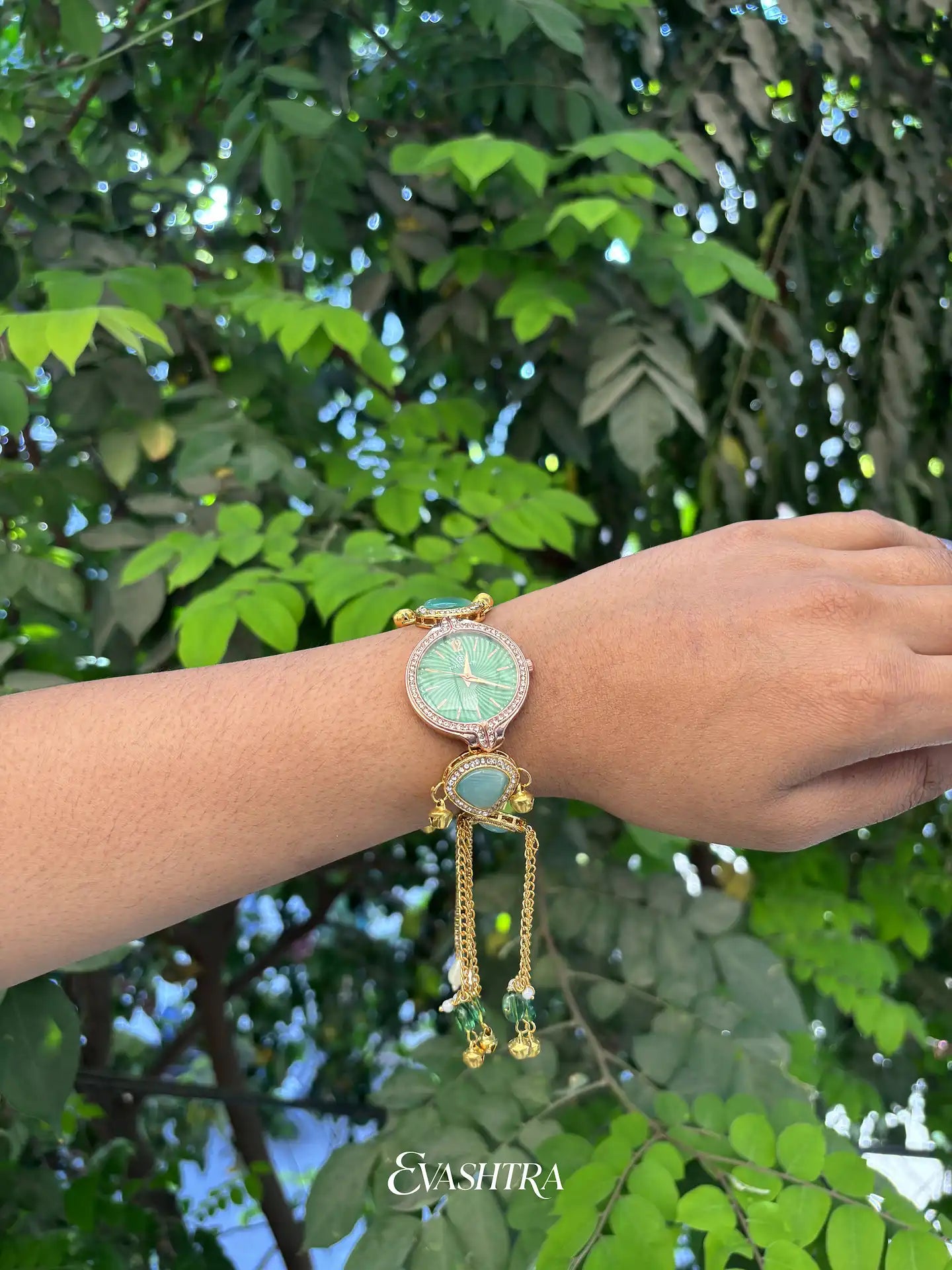 Wrist wearing a decorative watch with green face and gold accents against a leafy green background