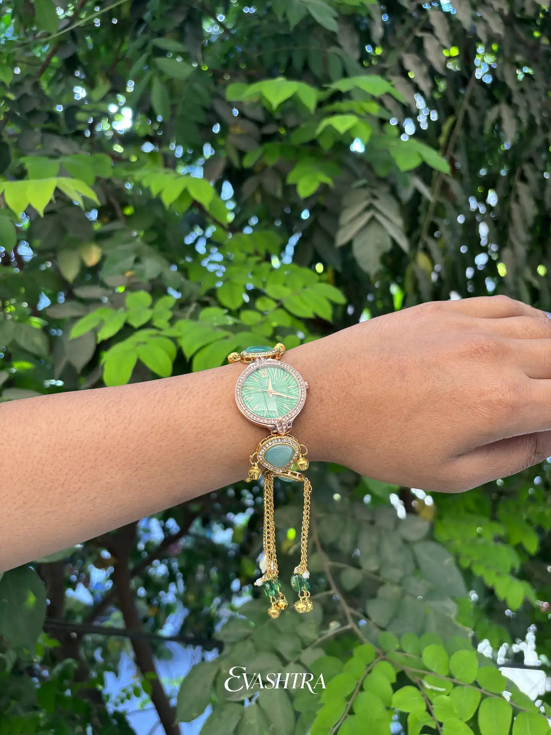Wrist wearing a decorative watch with green face and gold accents against a leafy green background