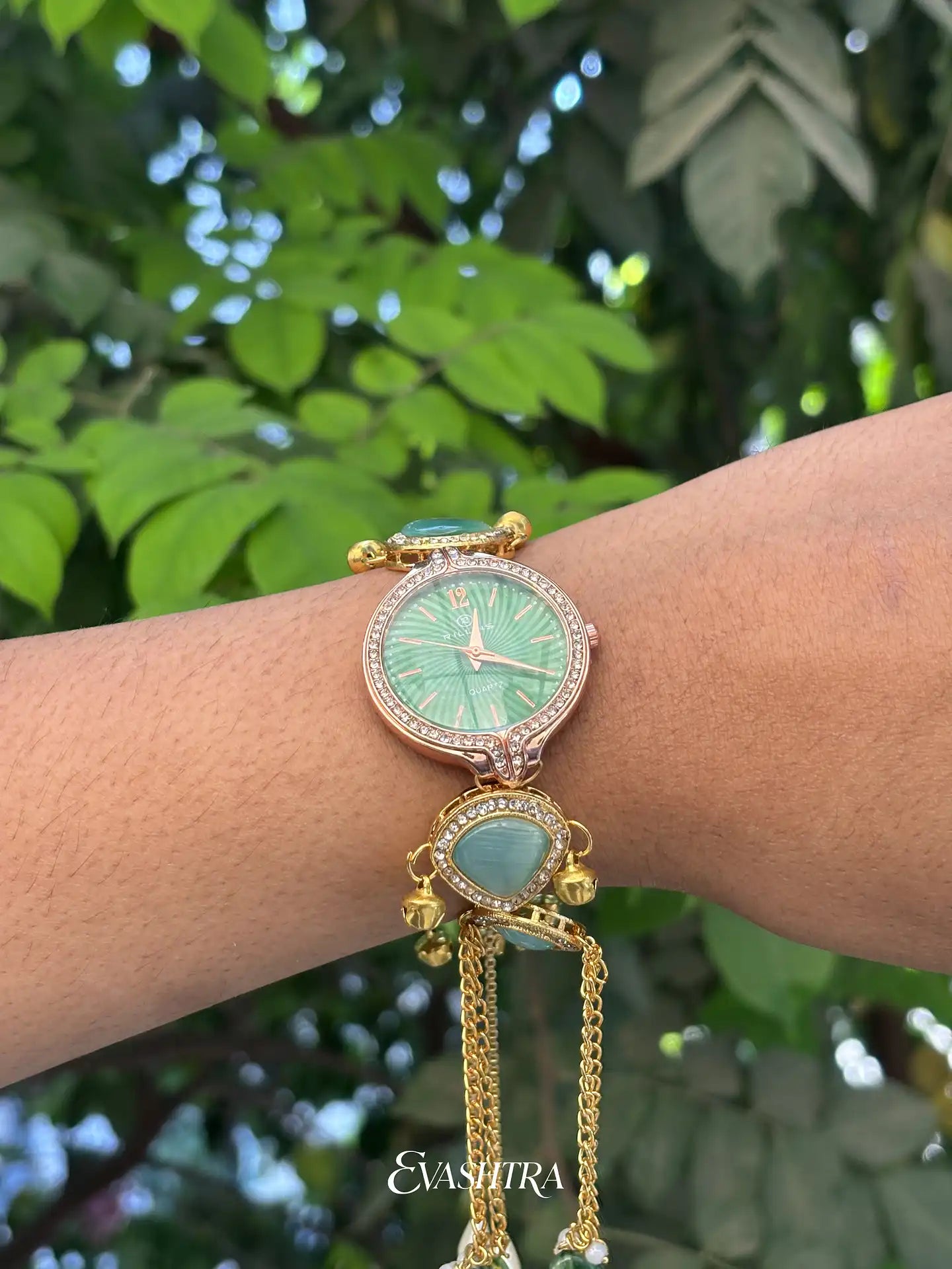 Gold wristwatch with green face on a wrist against a blurred green leafy background