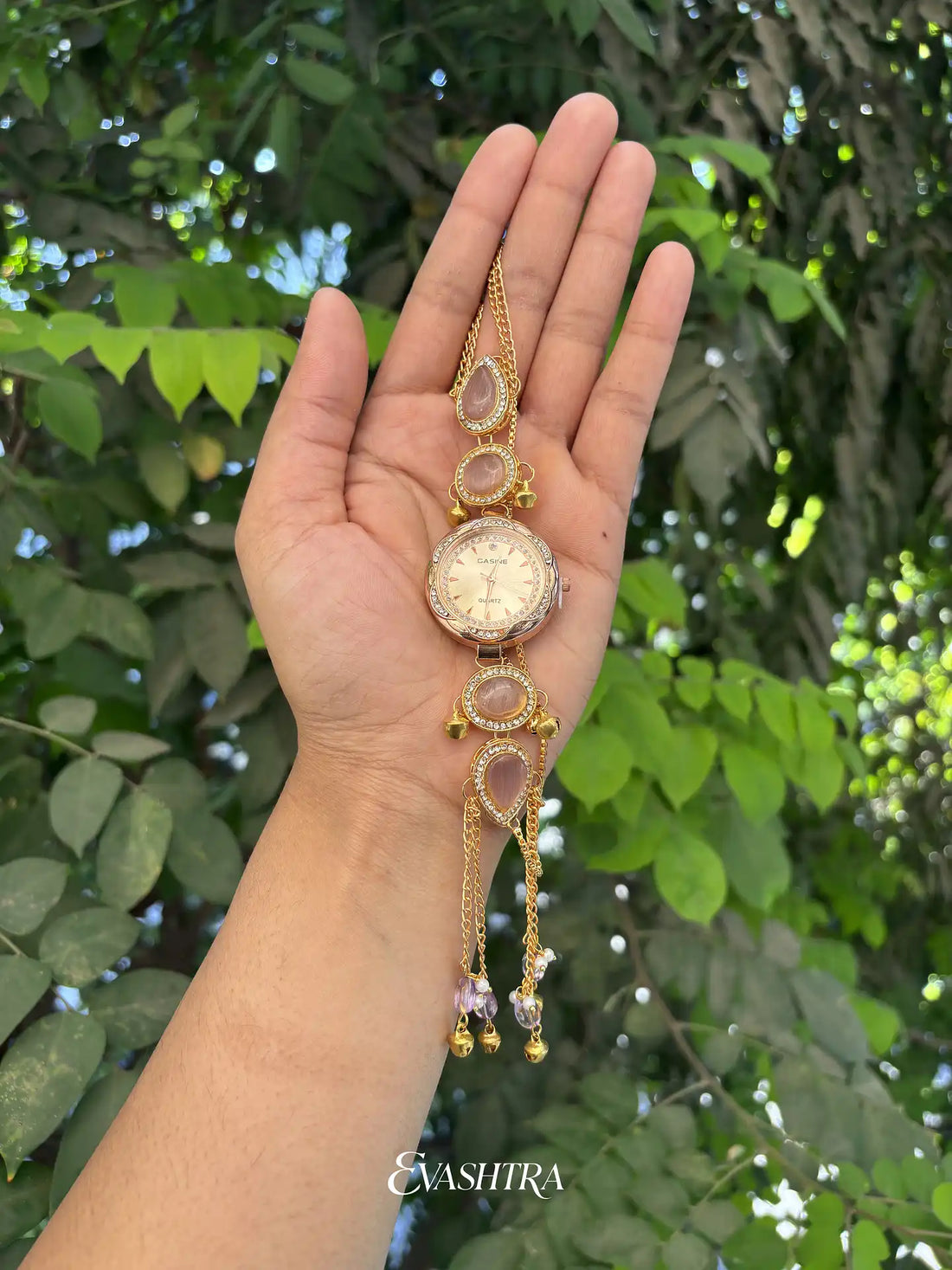 Gold necklace with a pendant held in a hand against a green leafy background