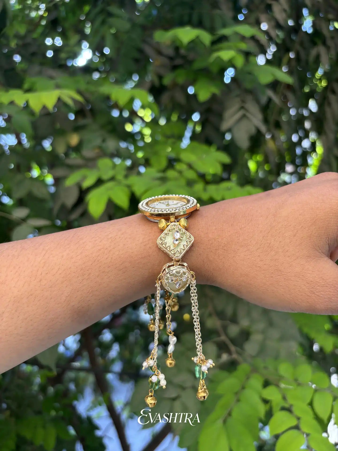 Gold bracelet with gemstones on a wrist against a green leafy background