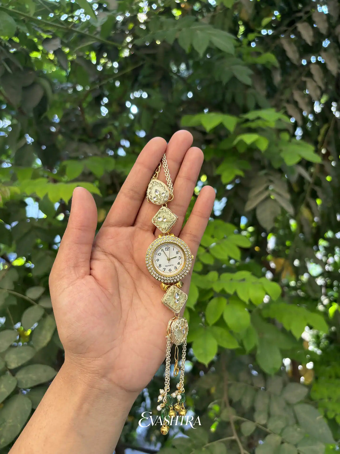 Hand holding a decorative watch with green foliage in the background