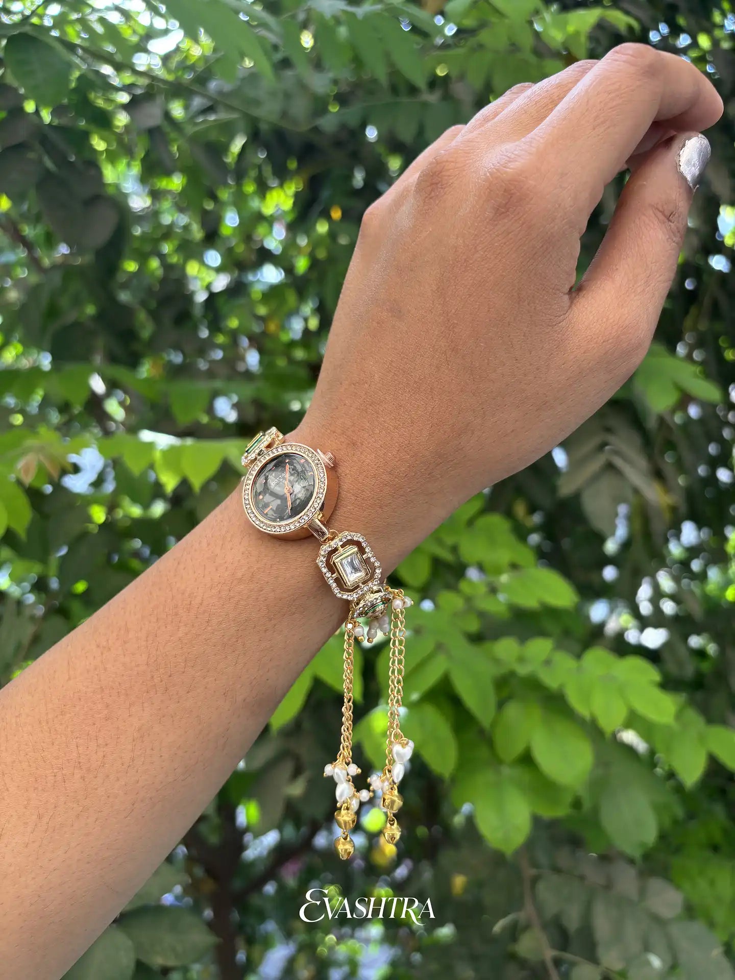 Hand wearing a decorative watch with green foliage in the background