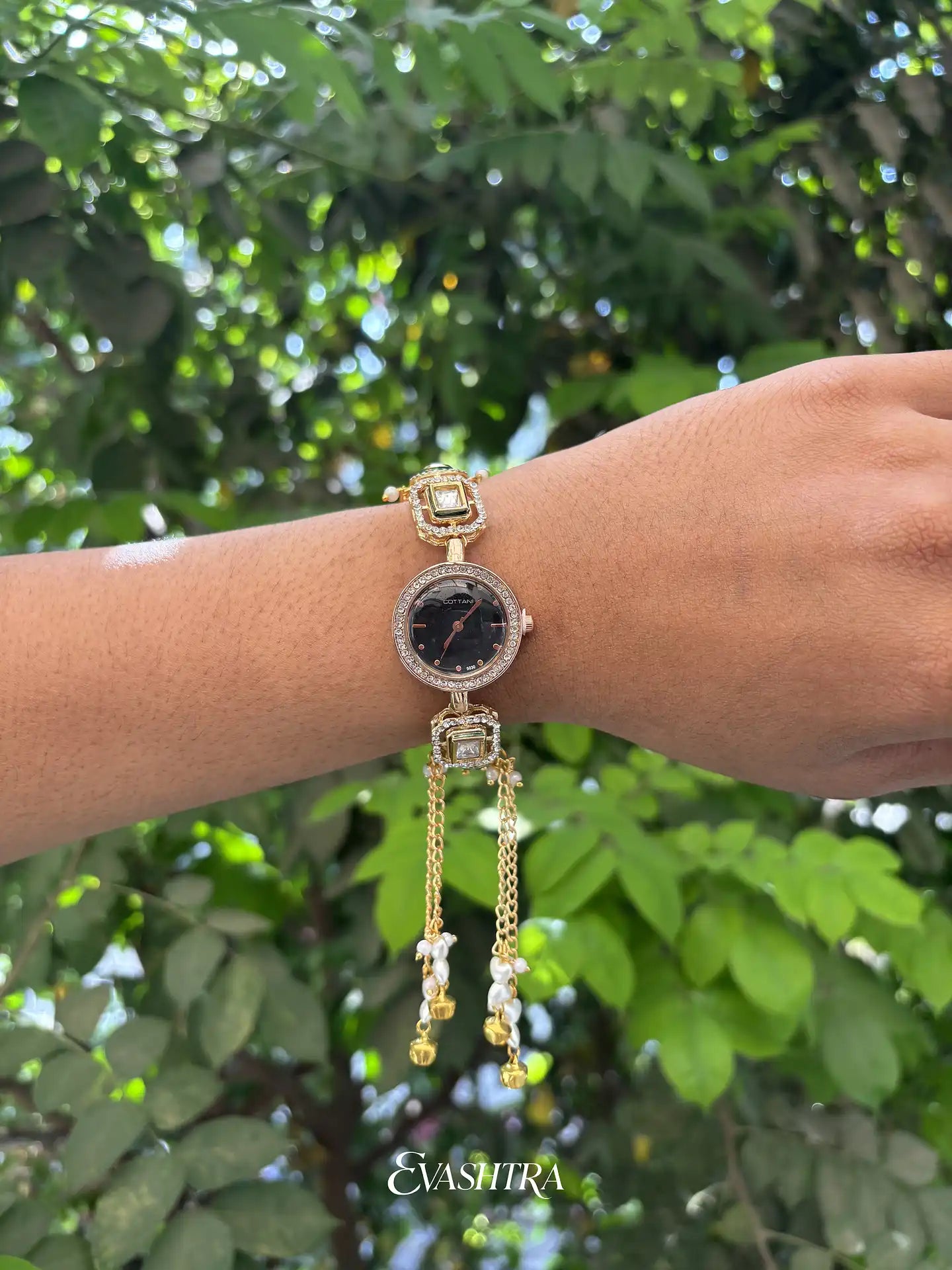 Gold bracelet with black watch face on wrist against a green leafy background
