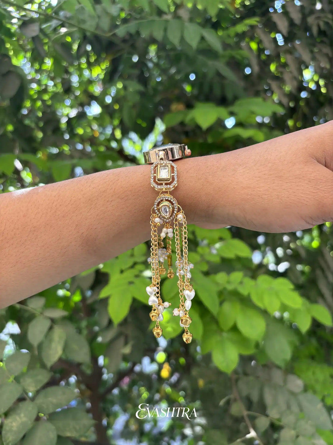 Gold bracelet with dangling elements on a wrist against a green leafy background
