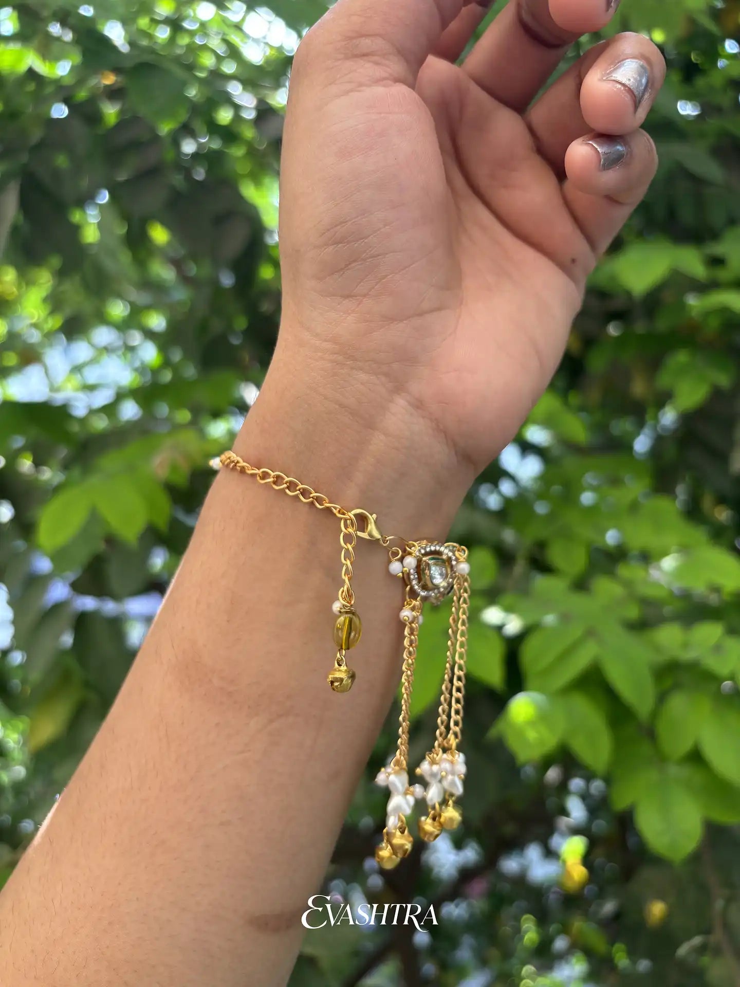 Gold bracelet with dangling charms on a wrist against a green leafy background