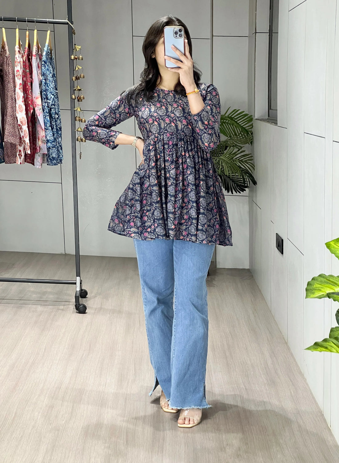 Person taking a mirror selfie wearing a floral top and blue jeans in a store.