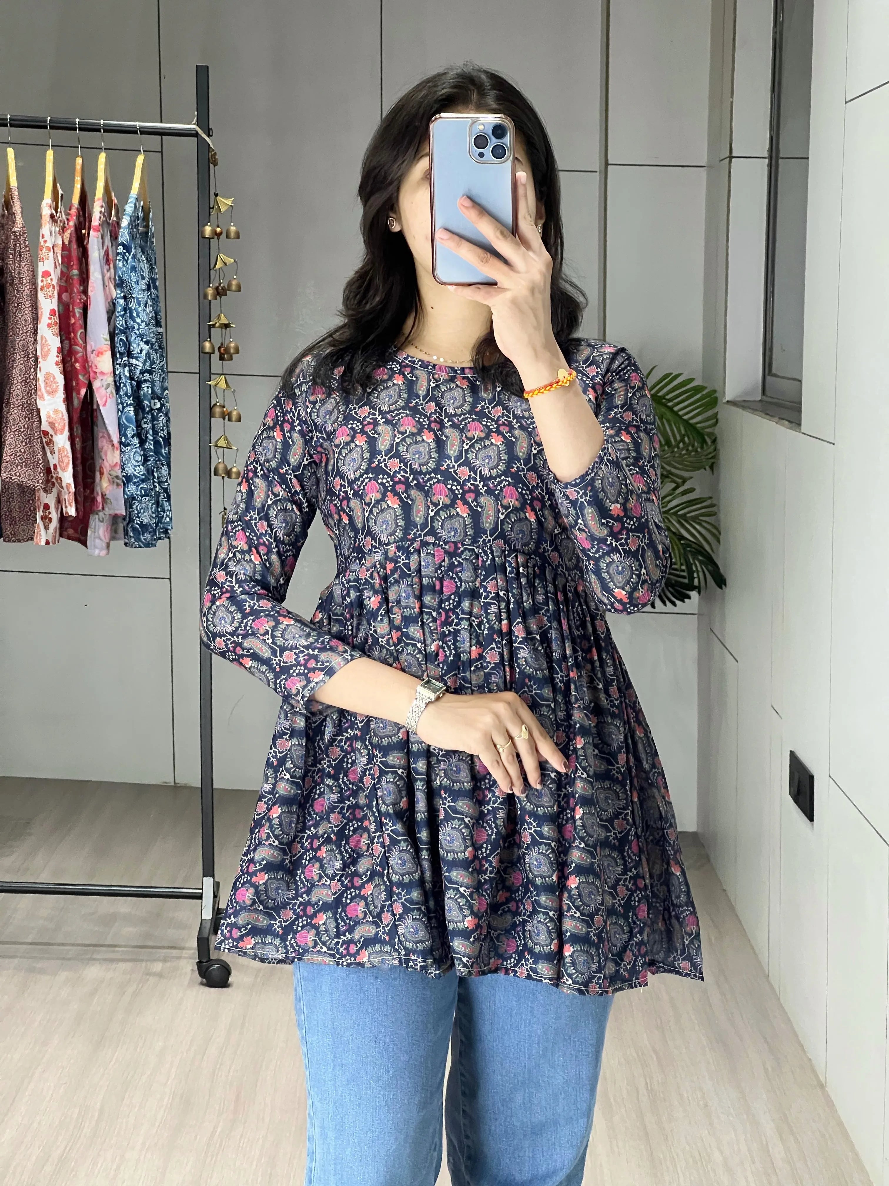 Person wearing a floral dress and blue jeans taking a mirror selfie.