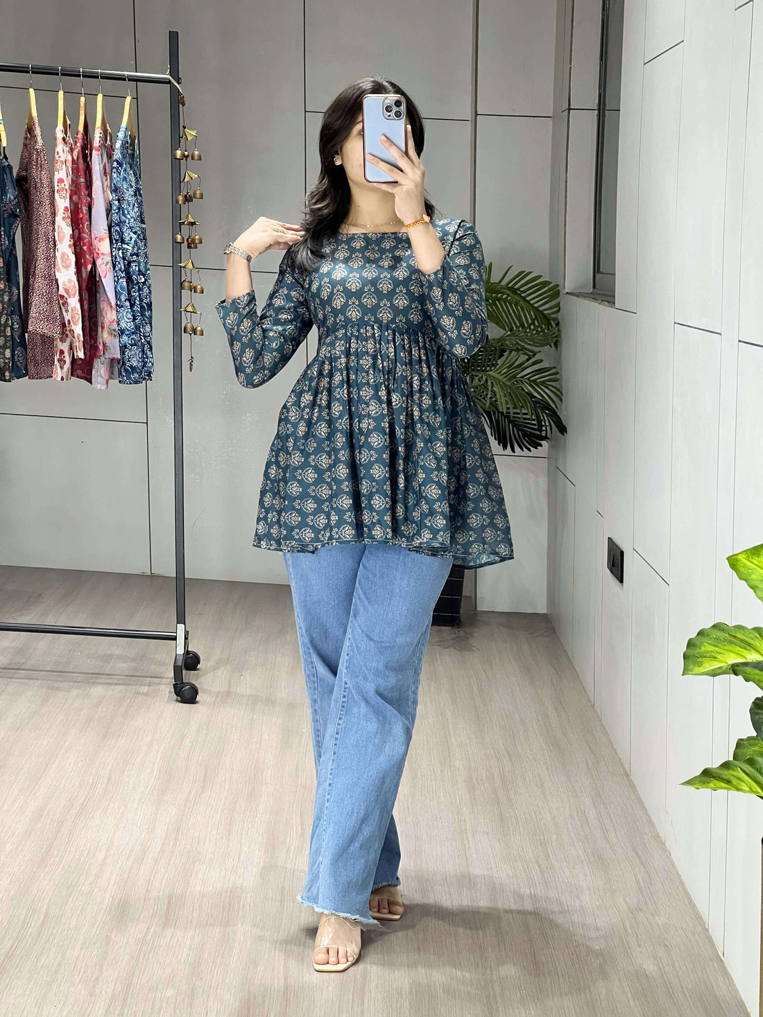 Woman taking a mirror selfie wearing a patterned top and blue jeans in a clothing store.
