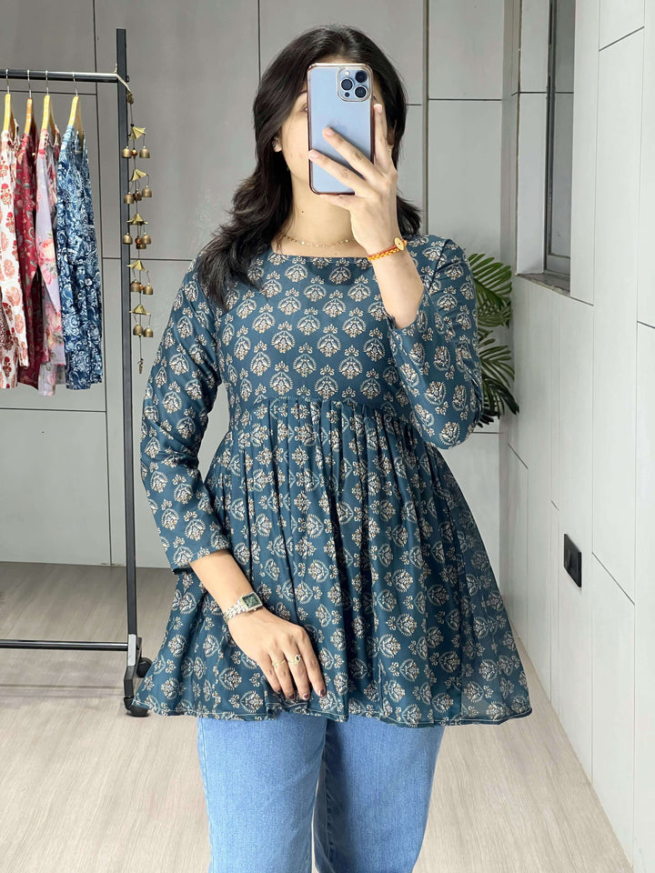 Person wearing a blue floral dress and blue jeans in a room with a clothing rack in the background.