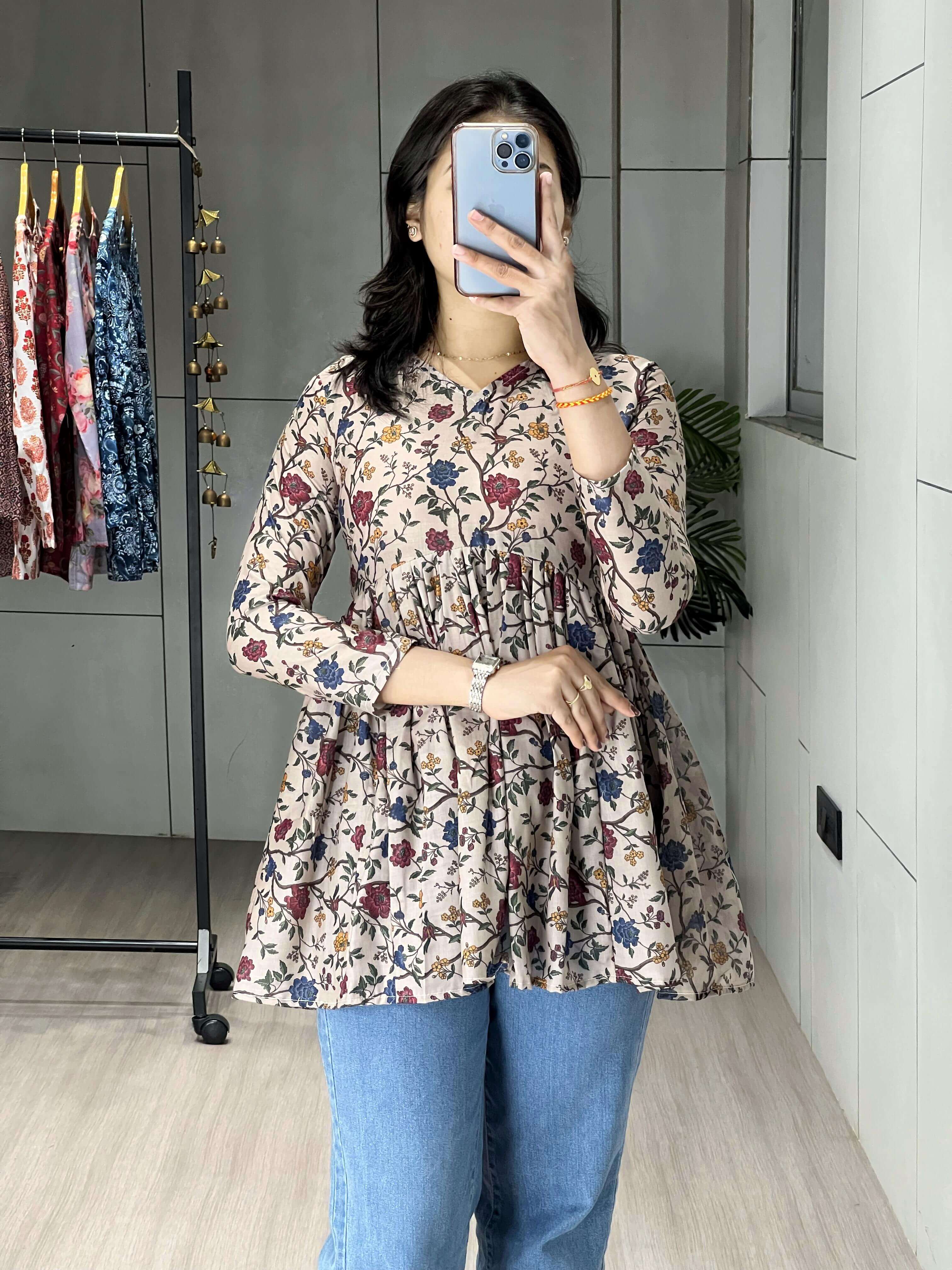Person wearing a floral dress and blue jeans taking a mirror selfie.