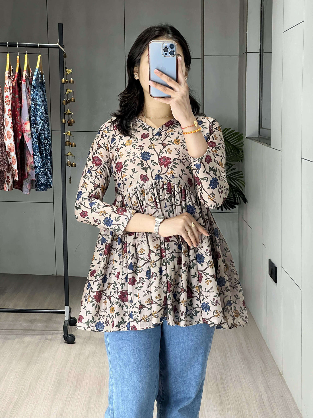 Person wearing a floral dress and blue jeans taking a mirror selfie.